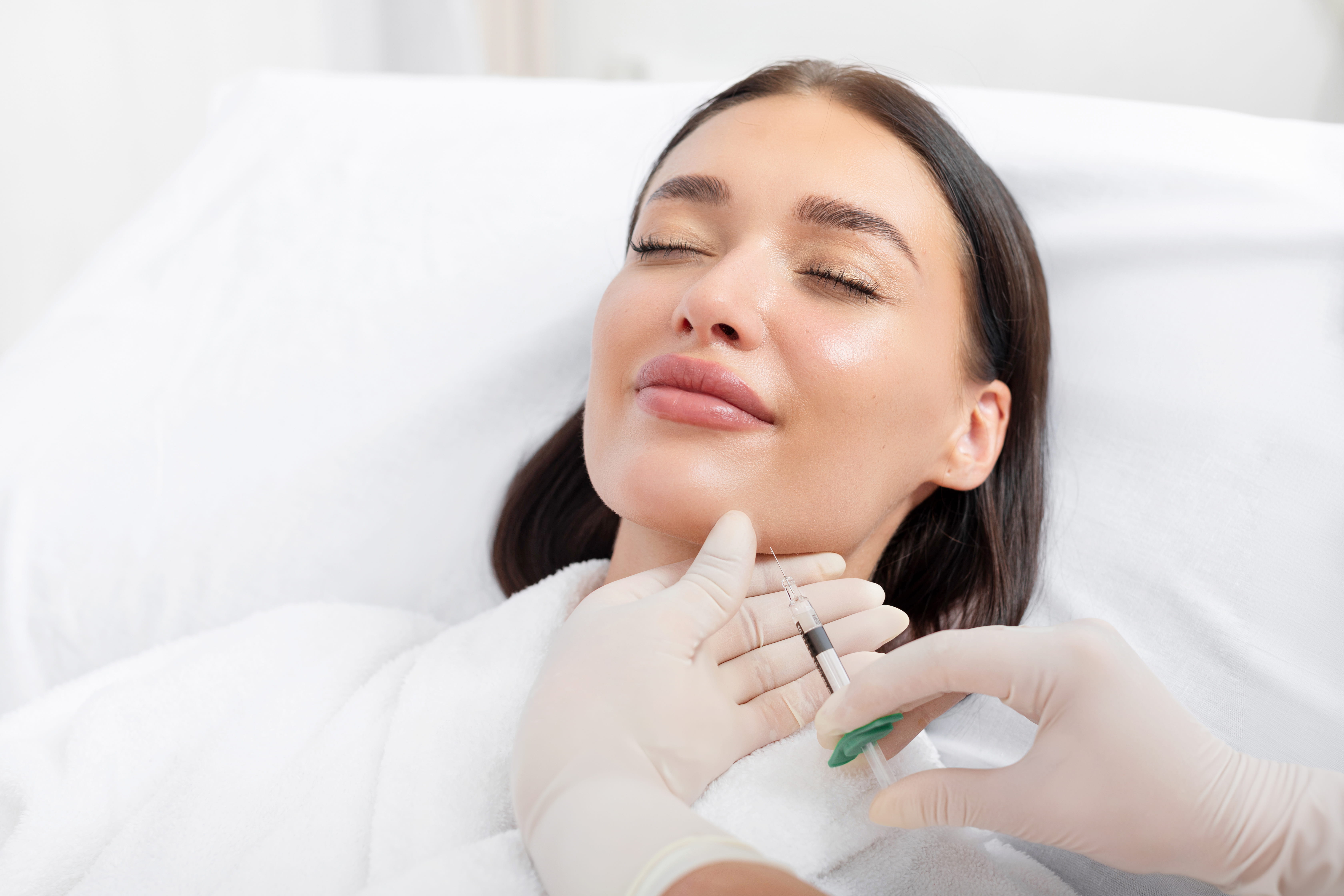 A woman receives a Kybella injection under her chin in a professional setting, highlighting non-surgical fat reduction options like Kybella and CoolSculpting