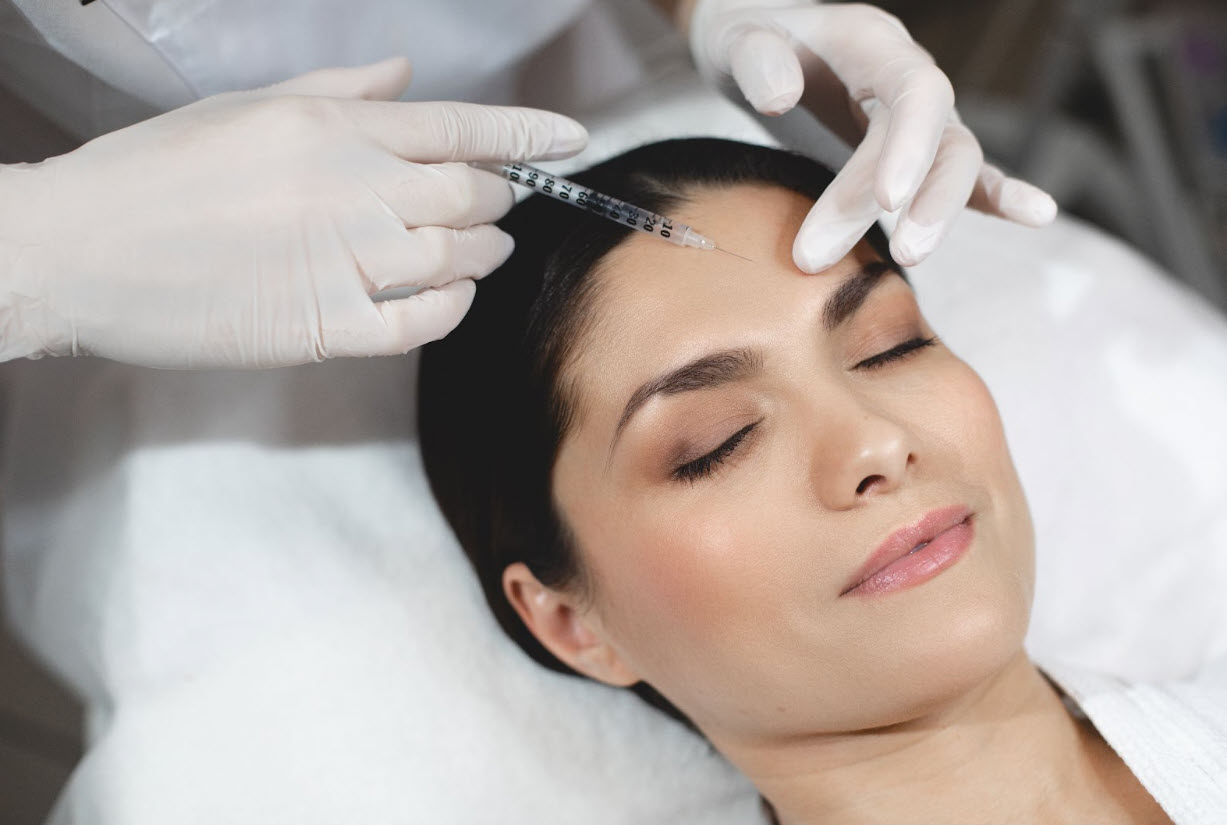 A professional performs a Botox injection on a woman's forehead to lift her brows, showcasing key things to know about a botox brow lift procedure.