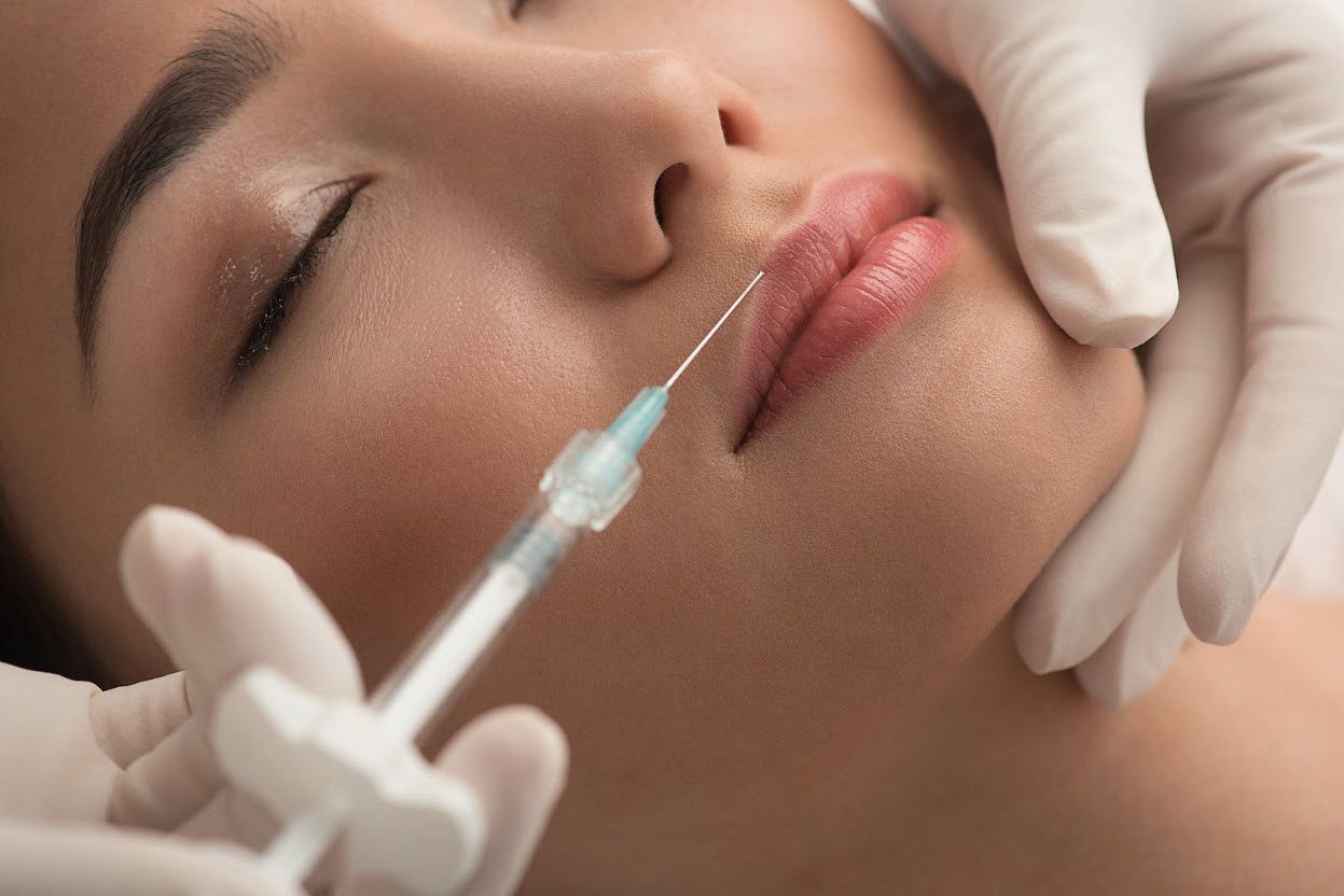 A woman with smooth, glowing skin gently touches her lips while smiling, symbolizing the natural enhancement results featured in a botox lip flip guide.